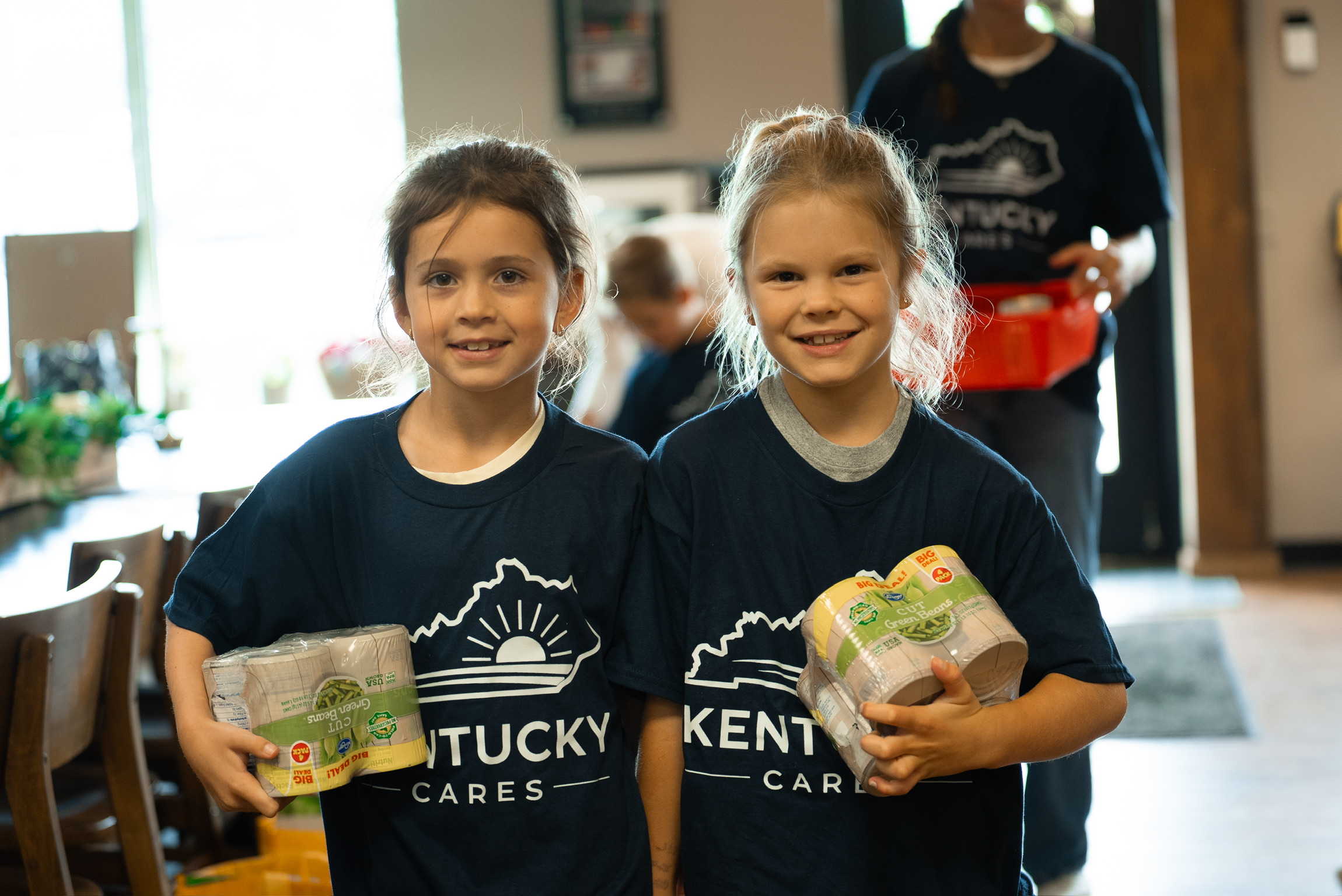 Two girls in Kentucky Cares shirts holding ingredients for the culinary class