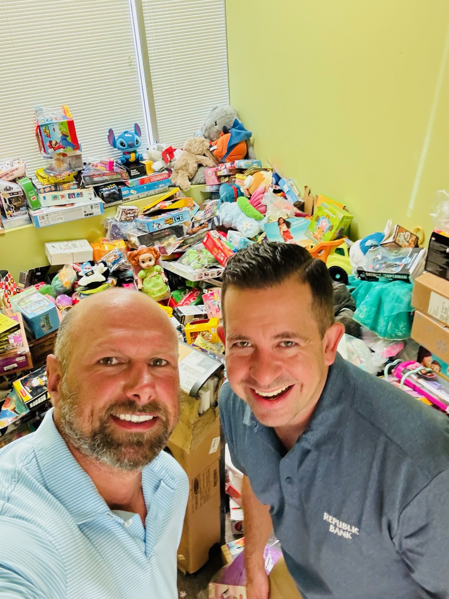 Two volunteers taking a selfie in front of a room full of donated toys