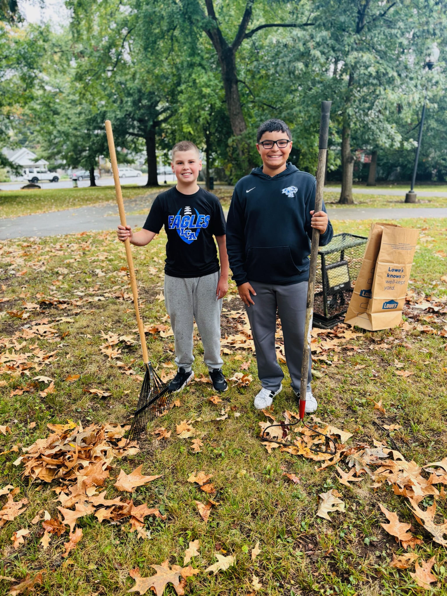 Two volunteers with rakes in a leaf-covered yard